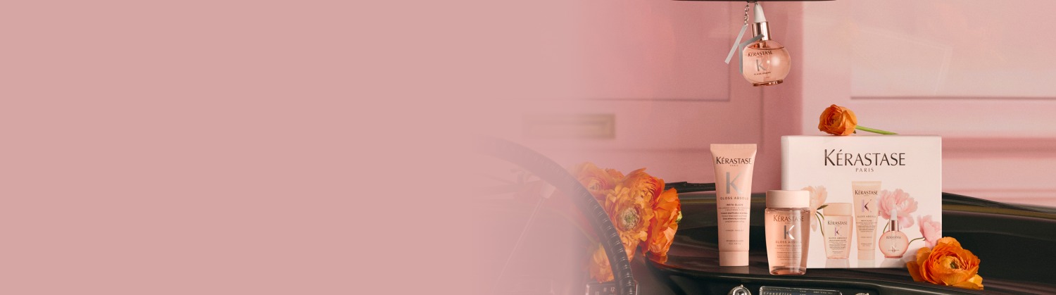 Bild von Kerastase-Haarpflegeprodukten, als Geschenk arrangiert, darunter mehrere goldene Flaschen, eine Duftkerze und eine weiße Frottee-Tasche, alles in festlicher weiß-goldener Verpackung auf hellem, weißem Hintergrund. Das Arrangement strahlt Luxus und Eleganz aus.​