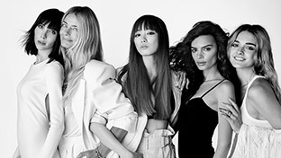 Fünf Frauen stehen in eleganten Outfits in Schwarz-Weiß, posieren selbstbewusst und lächeln leicht.