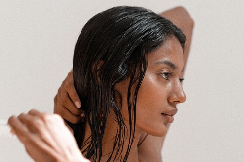 Porträt einer Frau mit dunklem, nassem Haar, die sich mit einer Hand durch die Haare fährt. Sanfter, heller Hintergrund.